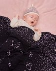 Ein Baby schläft zufrieden und ist zugedeckt mit einer personalisierten lilimoon Babydecke mit eingestricktem Sternenmuster und dem Sternzeichen Wassermann.
