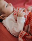 Ein Baby ist zugedeckt mit einer personalisierten lilimoon Babydecke gestrickt aus hochwertiger Baumwolle mit Kaschmir in rot und rosa.