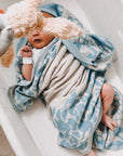 Ein neugeborenes Baby liegt kuschelig umhüllt von einer gestrickten lilimoon Babydecke in hellblau und cremeweiss mit Blütenmuster in einer Babywiege.