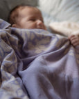 Ein schlafendes Baby im zugedeckt von einer kuscheligen lilimoon Babydecke in flieder und cremeweiss mit blütenmuster.