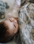 Ein Baby liegt zufrieden und zugedeckt mit einer kuscheligen lilimoon Babydecke in hellgrau und cremeweiss mit Blütenmuster in seinem Babybett.