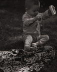 Ein kleiner Junge sitzt im Garten auf einer lilimoon Babydecke in schwarz und weiß mit Blütenmuster und spielt mit Holzspielzeug.
