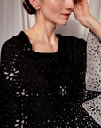Detail von gestricktem Cape in Schwarz mit hellgrauem Sternenmuster und eingestricktem Sternzeichen Krebs getragen von einer Frau.