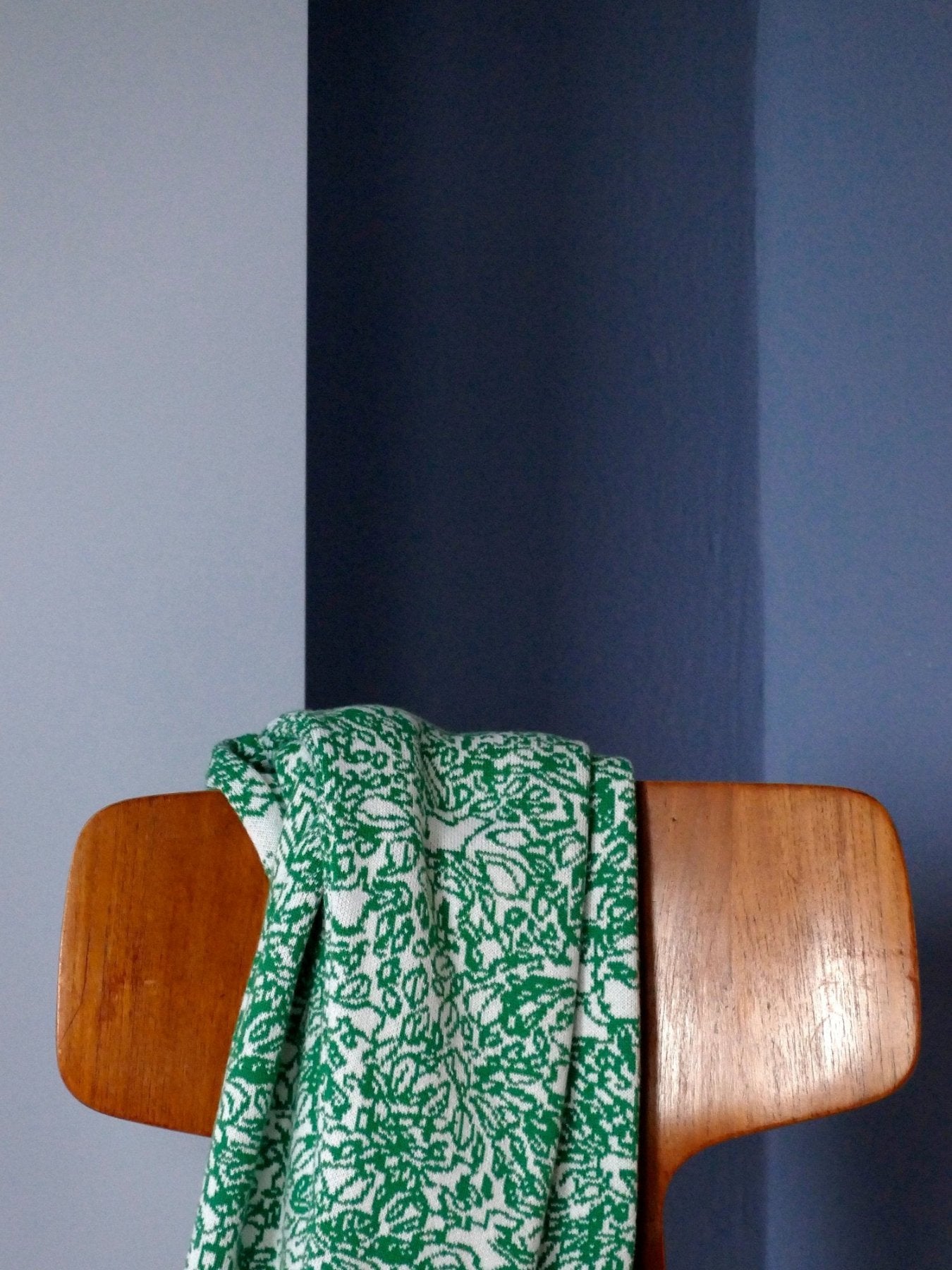 Strickjacke aus Baumwolle und Kaschmir von Mascha Iris Rotermund in weiß und grün hängt über einem Stuhl vor einer blauen wand.