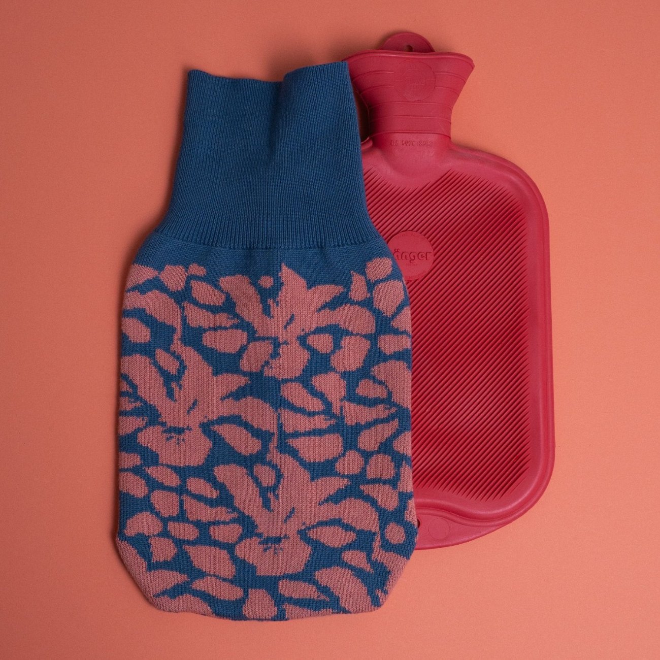 gestrickter Wärmflaschenbezug mit blütenmuster in blau und korallenrosa und rote Wärmflasche