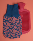 gestrickter Wärmflaschenbezug mit blütenmuster in blau und korallenrosa und rote Wärmflasche
