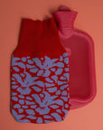 gestrickter wärmflaschenbezug mit blütenmuster in rot und flieder mit seperater roter wärmflasche