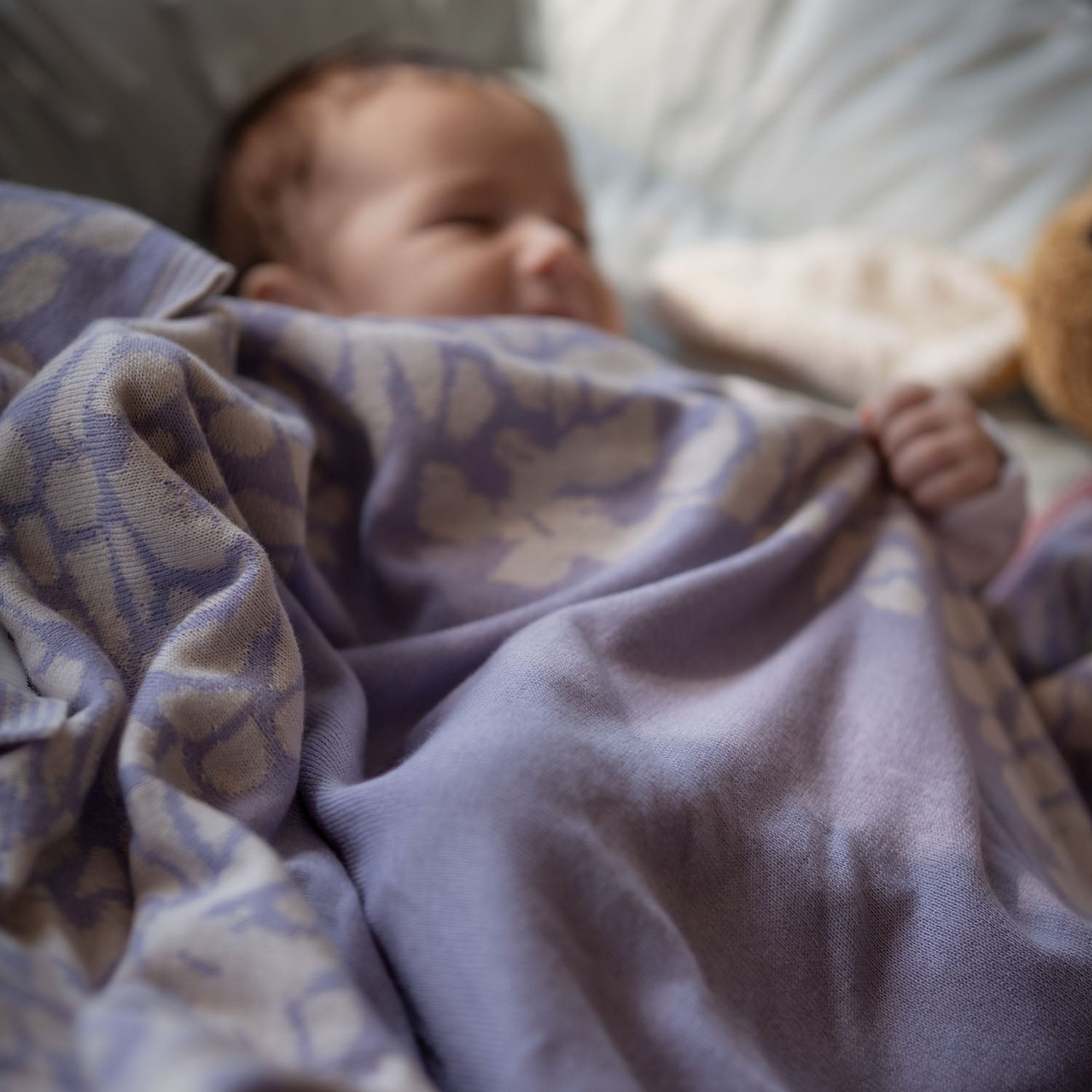 Ein schlafendes Baby im zugedeckt von einer kuscheligen lilimoon Babydecke in flieder und cremeweiss mit blütenmuster.